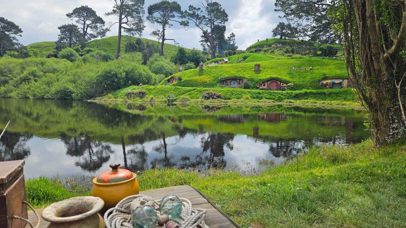 Blick über den See im Hobbiton Movie Set mit den kleinen Hobbit-Häusern und grünen Hügeln im Hintergrund.